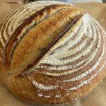Golden-brown same-day sourdough bread with a crisp crust and airy crumb, resting on a wooden surface.